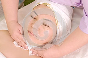 Beautician wipes the girl`s face. Young Asian woman in a beauty salon. Green algae facial mask