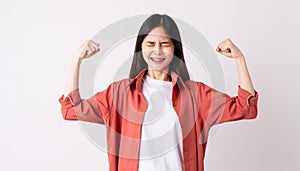 Young Asian woman with braces on teeth in toothy smile and raises arms and shows strong powerful.