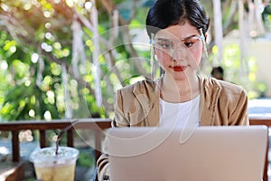 Young asian woman in business casual dress with face shield for healthcare, sitting in coffee shop and working on computer laptop