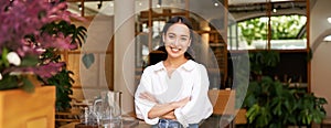 Young asian woman, cafe owner or manager, standing confident with arms crossed on hands, smiling and looking at camera
