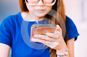 A young Asian woman in casual attire is using a smart phone indoor