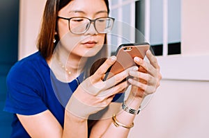 A young Asian woman in casual attire is using a smart phone indoor