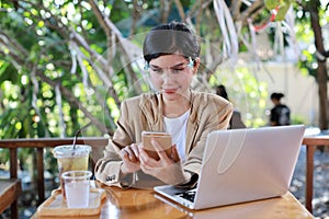 Young asian woman in casual dress with face shield for healthcare, sitting in coffee shop and using on smartphone and working on