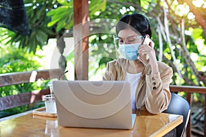 Young asian woman in casual dress with face shield and protect mask for healthcare, sitting in coffee shop and working on computer
