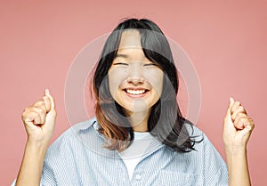 Young asian woman celebrates victory and success, feels lively and energetic over pink background