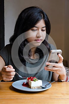 Young asian woman chating mobile phone with a cake