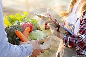 Young asian woman checking vegetable organic hydroponic farm and man harvest picking up fresh vegetable