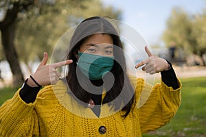 Young Asian woman in city park during covid19 - happy and pretty Korean girl in face mask standing on green grass during virus