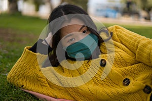 Young Asian woman in city park during covid19 - outdoors lifestyle portrait of happy and pretty Chinese girl in face mask lying