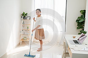 Young Asian woman cleaning floor at home doing chores with attractive smile on face