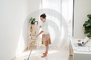 Young Asian woman cleaning floor at home doing chores with attractive smile on face