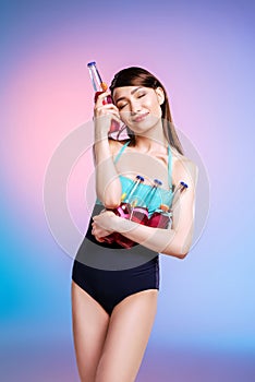 Young asian woman with closed eyes posing in swimsuit holding bottles with refreshing summer drinks