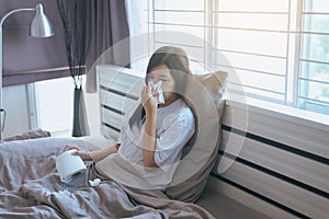 Young asian woman with cold blowing and runny nose on bed,sick female sneezing