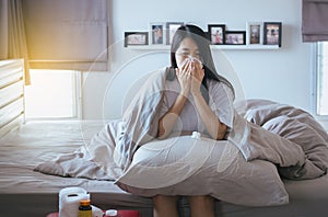 Young asian woman with cold blowing and runny nose on bed,sick female sneezing