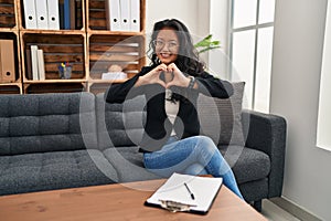 Young asian woman at consultation office smiling in love doing heart symbol shape with hands