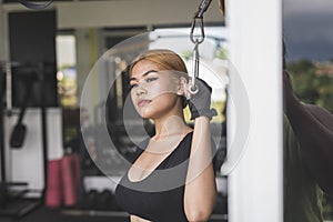 A young asian woman contemplates while holding onto a bar cable handle. In deep thought while at the gym