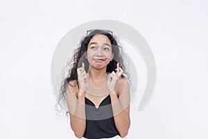 A young asian woman crosses her fingers while looking up, hoping and waiting anxiously for a great result. Isolated on a white