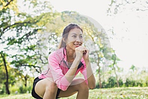 Young asian woman do squats for exercise to build up her beauty body in park environ with green trees. photo