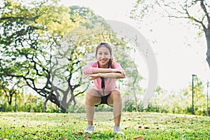 Young asian woman do squats for exercise to build up her beauty body in park environ with green trees. photo