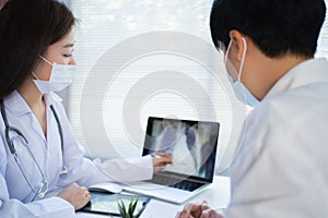Young Asian woman doctor wearing a prophylactic mask is explaining the x-ray of the lungs in a tablet of the patient