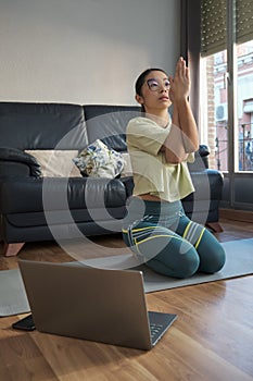 Young asian woman doing the hero pose with eagle arms at home.