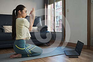 Young asian woman doing the hero pose with eagle arms at home.