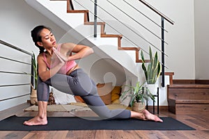 Young asian woman doing low lunge twist yoga pose at home. Parivrtta anjaneyasana home yoga practice.