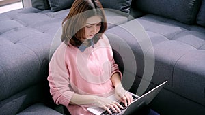 Young asian woman doing research work for her business. Smiling woman sitting on sofa relaxing while browsing online shopping.