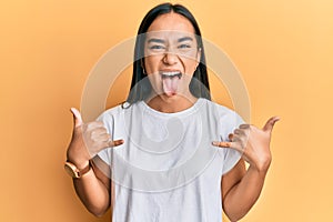 Young asian woman doing shaka sign with hands sticking tongue out happy with funny expression