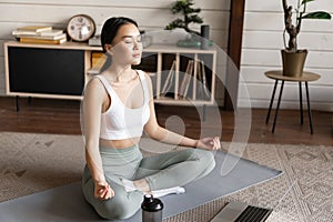 Young asian woman doing yoga with laptop, listening to meditation instructor on application or website, doing meditating