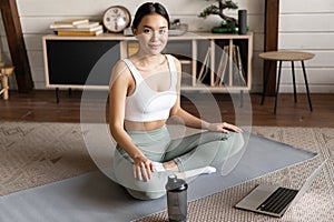 Young asian woman doing yoga with laptop, listening to meditation instructor on application or website, doing meditating
