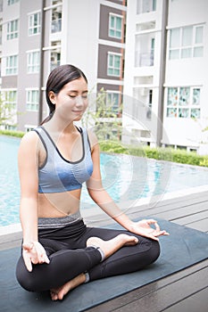 Young asian woman doing yoga moves or meditating by the pool,