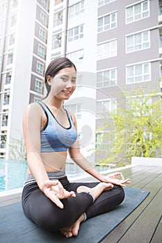 Young asian woman doing yoga moves or meditating by the pool,