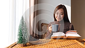 A young asian woman drinking coffee while reading book at home