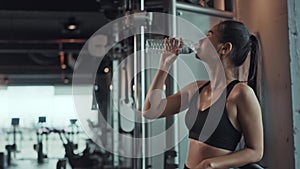 Young asian woman drinking water from bottle during workout in gym. Fitness athlete beautiful girl wearing sportswear with tired