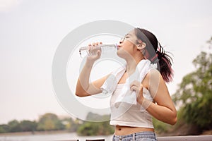 A young Asian woman drinks from a water bottle, cooling down after walking outdoors in a hot day