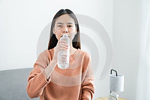 Young Asian woman drinks water from a bottle at home.