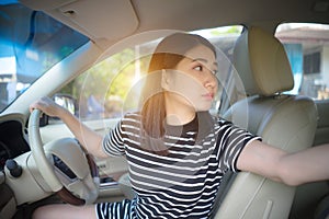 Young Asian woman driving car keeps wheel turning around looking back over shoulder check behind going reverse.