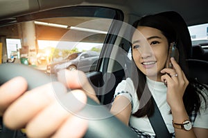 Young Asian woman driving car and talking on cell phone with smiling face on the road