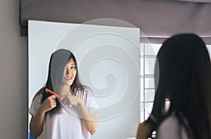 Young asian woman drying her long hair with dryer or comb front of mirror