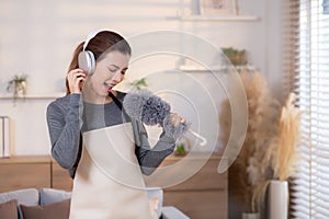 Young asian woman dusting while listening to music with headphones in a bright, organized.