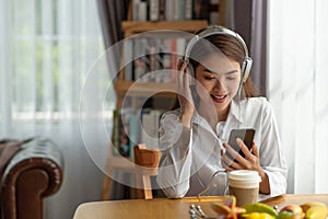 Young Asian woman enjoy listening to music with headphones and a hot cup of coffee on the table, happy and relaxing time
