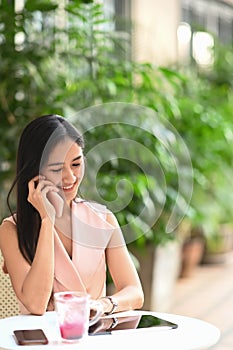 Young Asian woman entrepreneur sitting at outdoor cafe and talking on mobile phone.