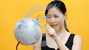 Young asian woman examining the globe with a magnifying glass