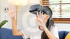 Young asian woman exciting in VR headset looking up and trying to touch objects in virtual reality at home living room, Teenager