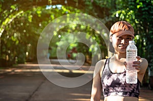 Young asian woman in exercise uniform holding water bottle show in hand ready to workout in green nature blurry backgound