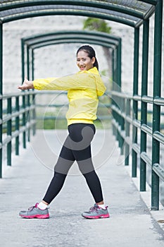 Young asian woman exercising outdoor in yellow neon jacket, stretching