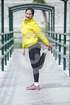 Young asian woman exercising outdoor in yellow neon jacket, stretching