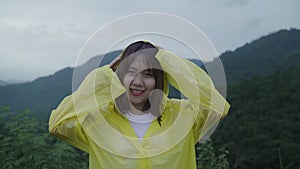 Young Asian woman feeling happy playing rain while wearing raincoat walking near forest.