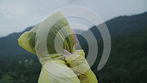 Young Asian woman feeling happy playing rain while wearing raincoat walking near forest.